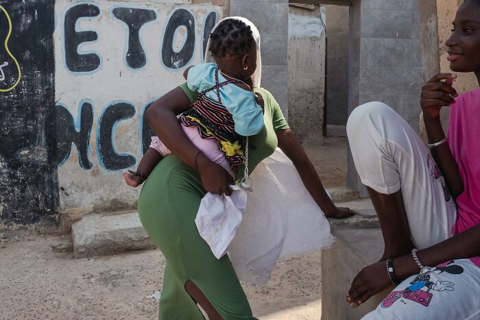 African child carried by woman in green dress with another child nearby, part of powerful photographs of children of the world.