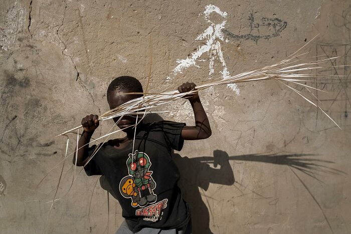 Child in colorful shirt holding sticks against a textured wall, a powerful photograph of children of the world by Andrea Torrei