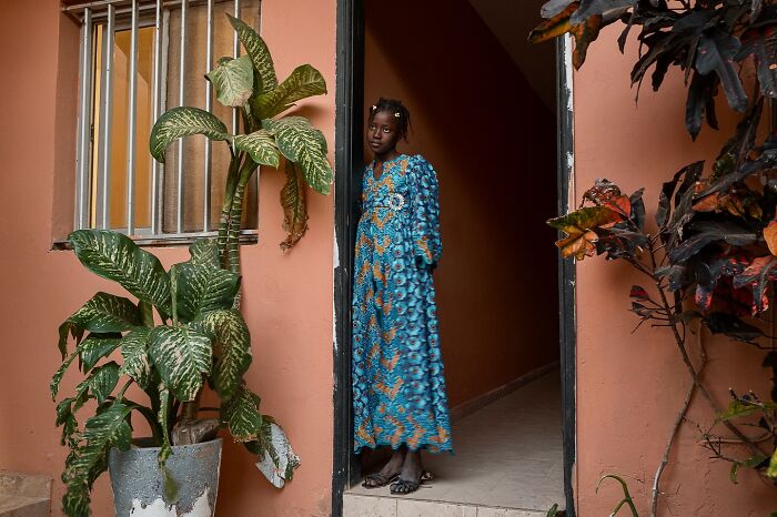 Young girl in a blue patterned dress standing in a doorway, representing children of the world in powerful photography.