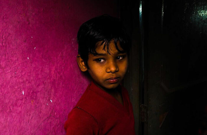 Young boy standing against a vibrant pink wall, captured in a powerful photograph from children of the world series.