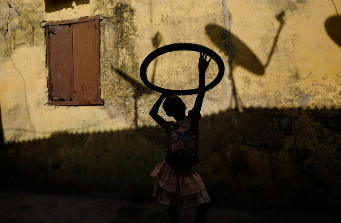 Silhouetted child playing with hoop against textured wall, capturing powerful children of the world photograph by Andrea Torrei
