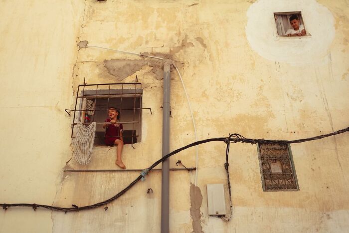 Two children on windows of an old building, captured in a powerful photograph of children of the world by Andrea Torrei.