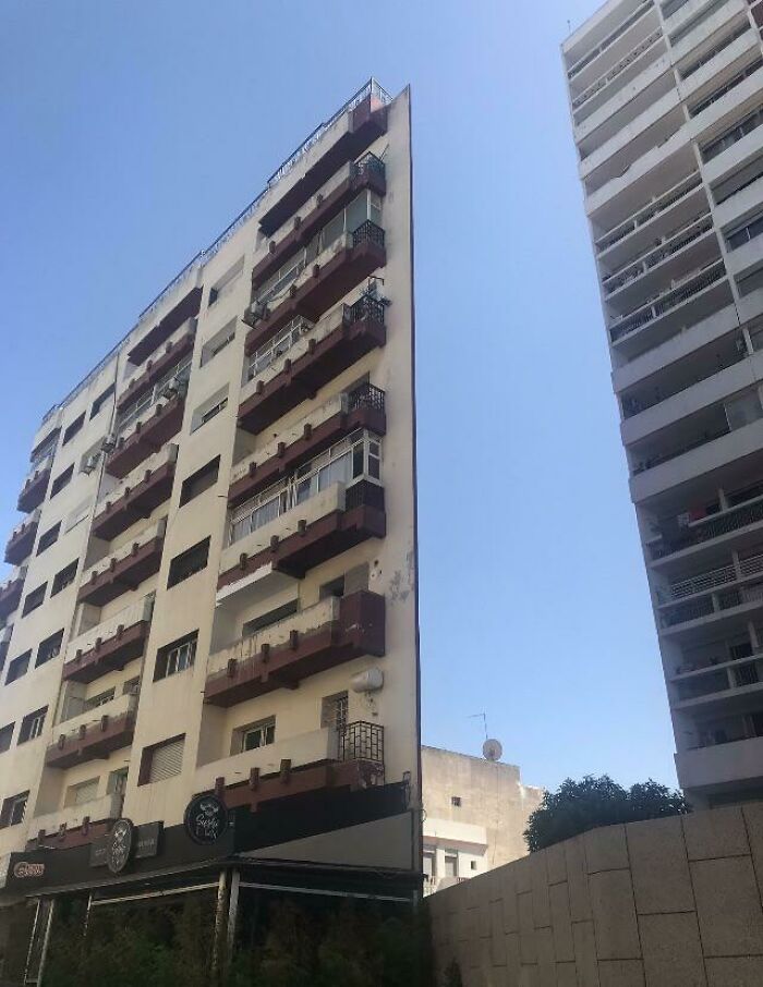 Narrow building with balconies creating a weird, blessed and cursed visual effect against clear blue sky.