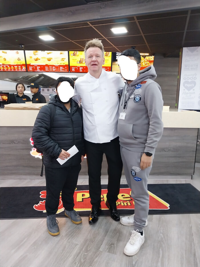 Two men posing with a man dressed as a celebrity chef in a fast food restaurant, a funny celebrity look-alike moment.
