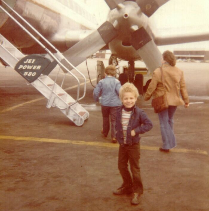 Vintage vacation pic showing a smiling child and family boarding an old airplane before cell phones had cameras.