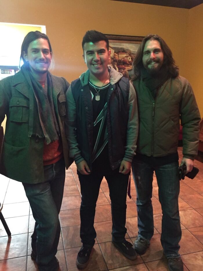 Three men standing indoors posing for a photo with a celebrity lookalike in a casual setting, Johnny Derp style.