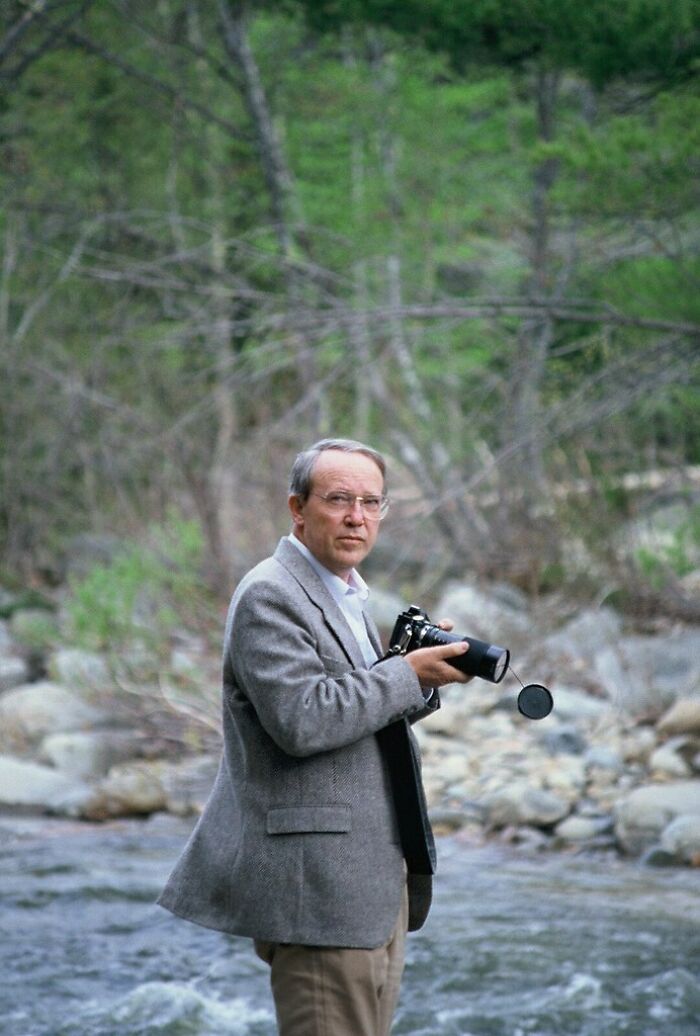 Man holding a vintage camera by a river in nature, capturing vacation pics from a time before cell phone cameras existed