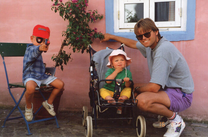 Young family on vacation captured in a candid moment with vintage stroller, casual clothing, and a playful child with a toy gun.