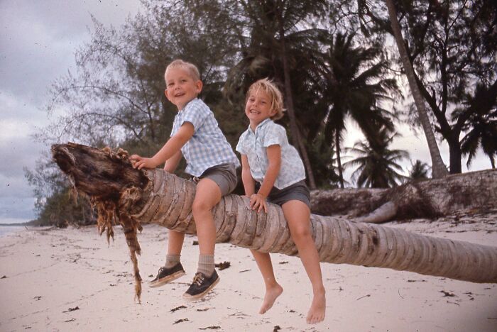 Two children playing on a fallen palm tree on a sandy beach in a vintage vacation pic before cell phones had cameras
