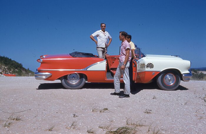 Three men standing by a vintage convertible car in a desert landscape, vacation pics from before cell phone cameras.