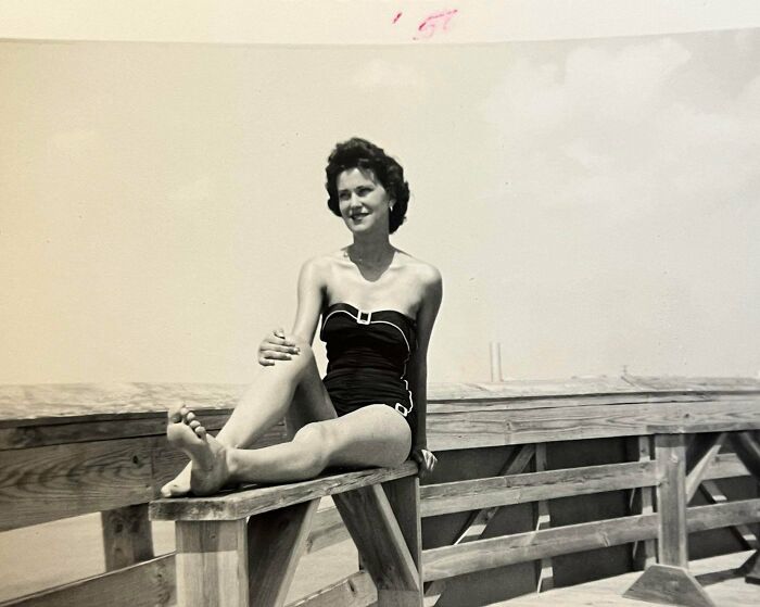 Vintage vacation photo of a woman in a swimsuit sitting on a wooden railing before cell phones had cameras.