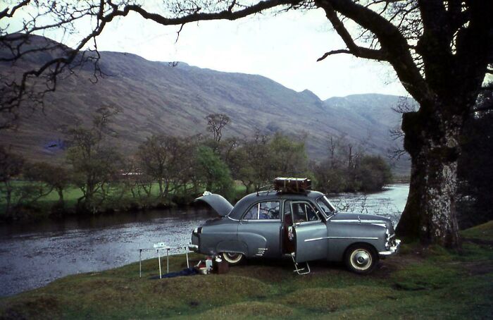 Vintage vacation car parked by a river in a scenic mountain landscape, capturing nostalgic vacation pics before cell phone cameras.