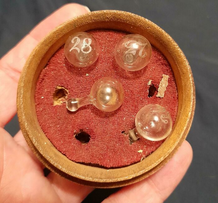 Hand holding a round container with old, numbered glass marbles and vintage objects found and unidentified by people.