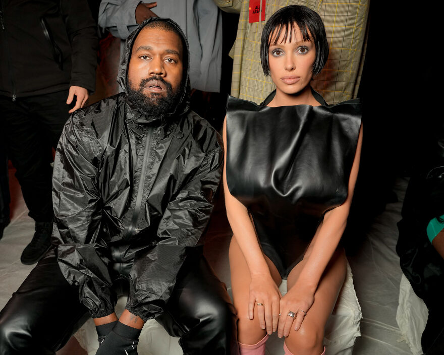 Kanye West and Bianca Censori sitting together at an event, showcasing fashion linked to West&rsquo;s growing empire.