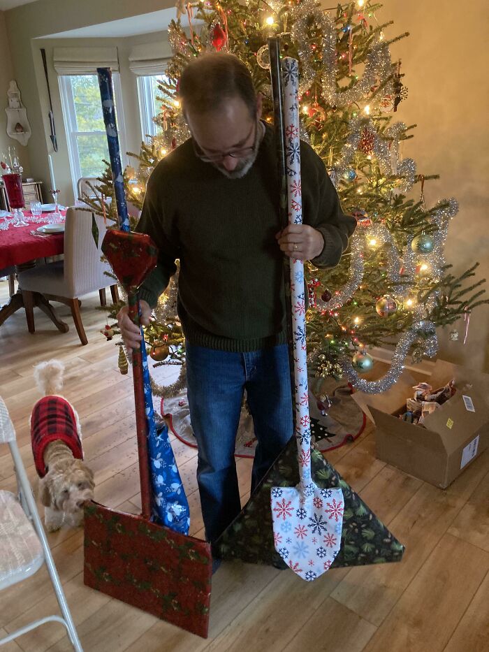 Man holding Christmas-themed shovels in a decorated living room with a tree, showcasing funny and wholesome parent moments.