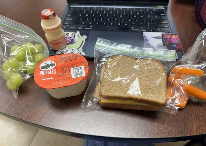 Packed lunch with sandwich, grapes, carrots, yogurt drink, and original Pringles showing funny and wholesome parents' care for kids.