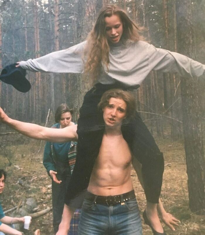 A young man carrying a woman on his shoulders in a forest, showcasing funny and wholesome moments parents share with kids.