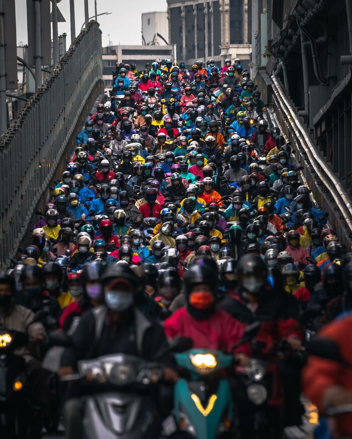 Dense crowd of motorcyclists wearing colorful jackets and helmets, showcasing everyday life in Asia urban traffic scene.