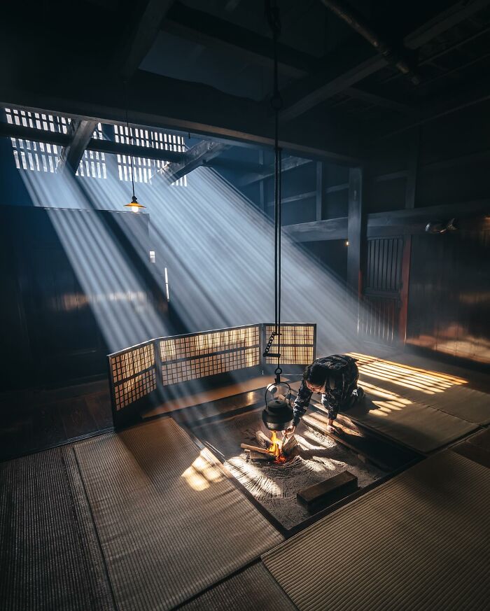 Traditional Asian interior with sunlight streaming through windows as a person tends to a small fire in the hearth.