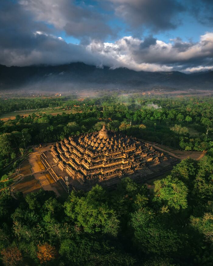 Ancient temple surrounded by dense green forest under dramatic clouds, showcasing glimpses of everyday life in Asia.