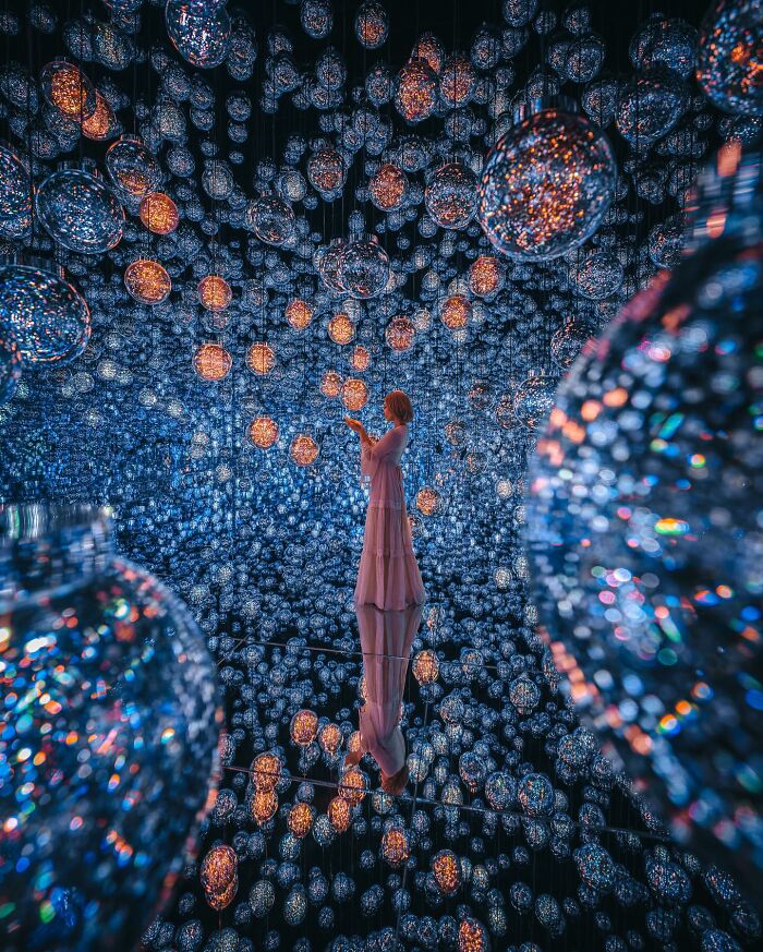 A woman in a flowing dress explores an art installation with countless glowing orbs reflecting everyday life in Asia.