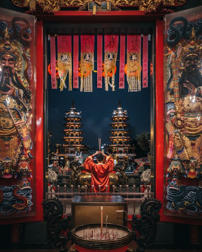 Man in red robe praying inside ornate Asian temple with pagodas in the background, showcasing everyday life in Asia.