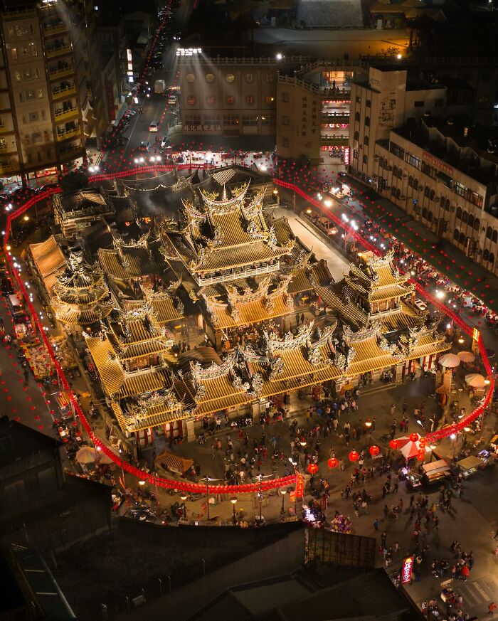 Night aerial view of an illuminated traditional Asian temple surrounded by crowds, showcasing glimpses of everyday life in Asia.