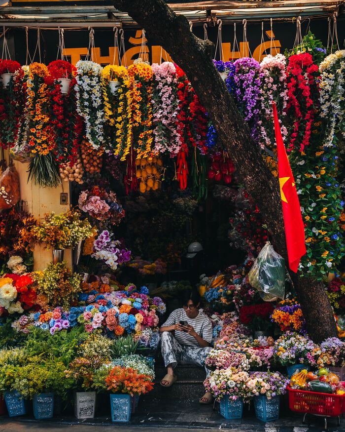 Flower vendor surrounded by vibrant blooms at an Asian street market, capturing everyday life in Asia.