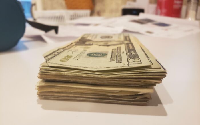 Stack of US dollar bills on a table with a blurred background, illustrating funny and wholesome parent moments shared by kids.