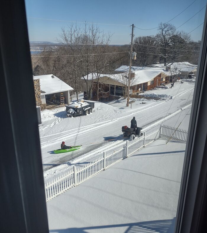 Parent pulling child on kayak through snowy neighborhood, showcasing funny and wholesome moments shared by kids.