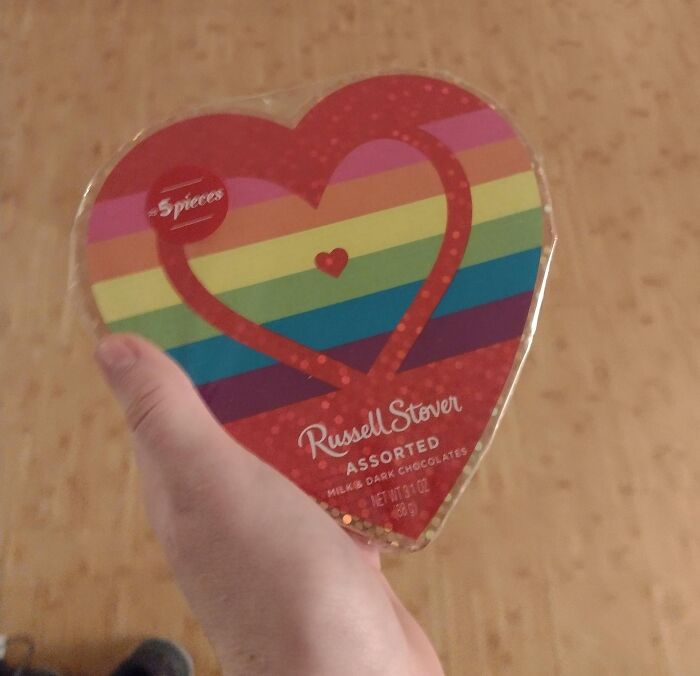 Hand holding a heart-shaped Russell Stover assorted chocolates box with rainbow stripes, showing funny and wholesome parents.