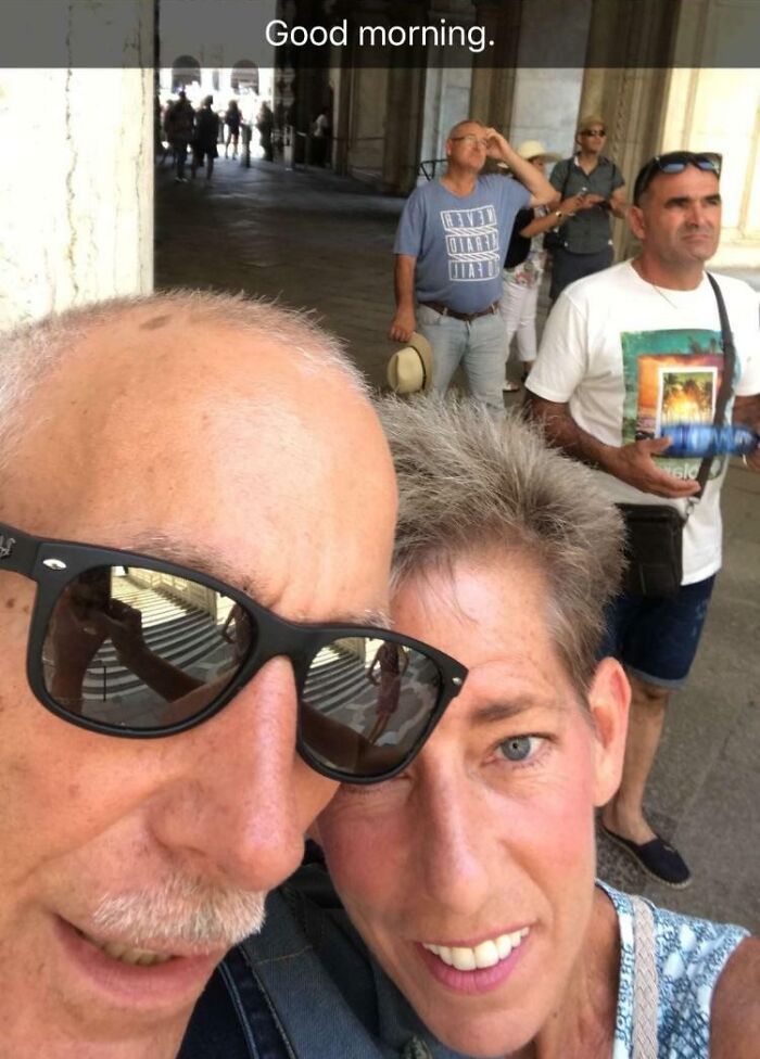 Close-up selfie of funny and wholesome parents sharing a lighthearted moment in a public outdoor area.
