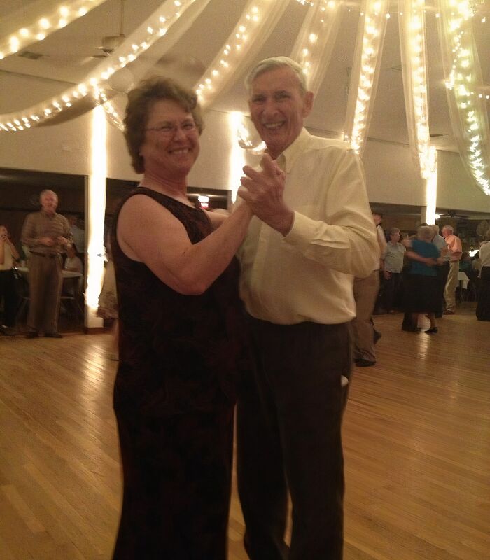 Older couple smiling and dancing at a warmly lit event, capturing a wholesome moment parents and kids love to share.