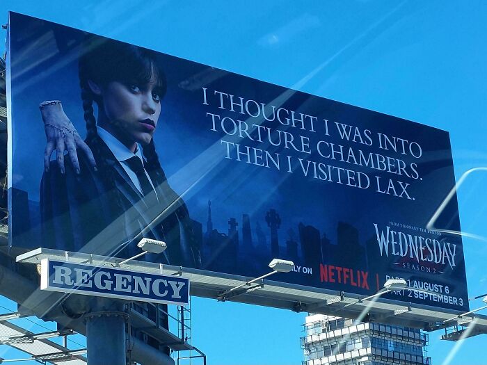 Funny and weird billboard featuring a dark-themed promotion for Netflix's Wednesday season 2 with a sarcastic message.