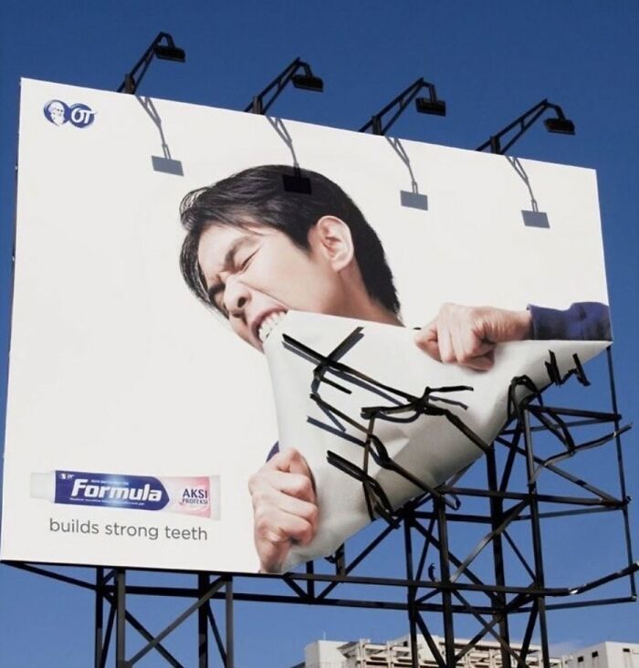 Billboard showing a man biting a bent megaphone, creatively advertising toothpaste that builds strong teeth.