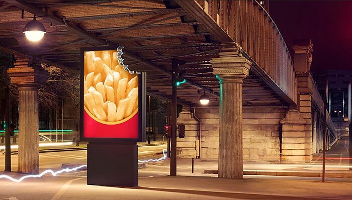 Billboard shaped like a bitten container of fries on a city street, showcasing a funny and weird advertising concept.