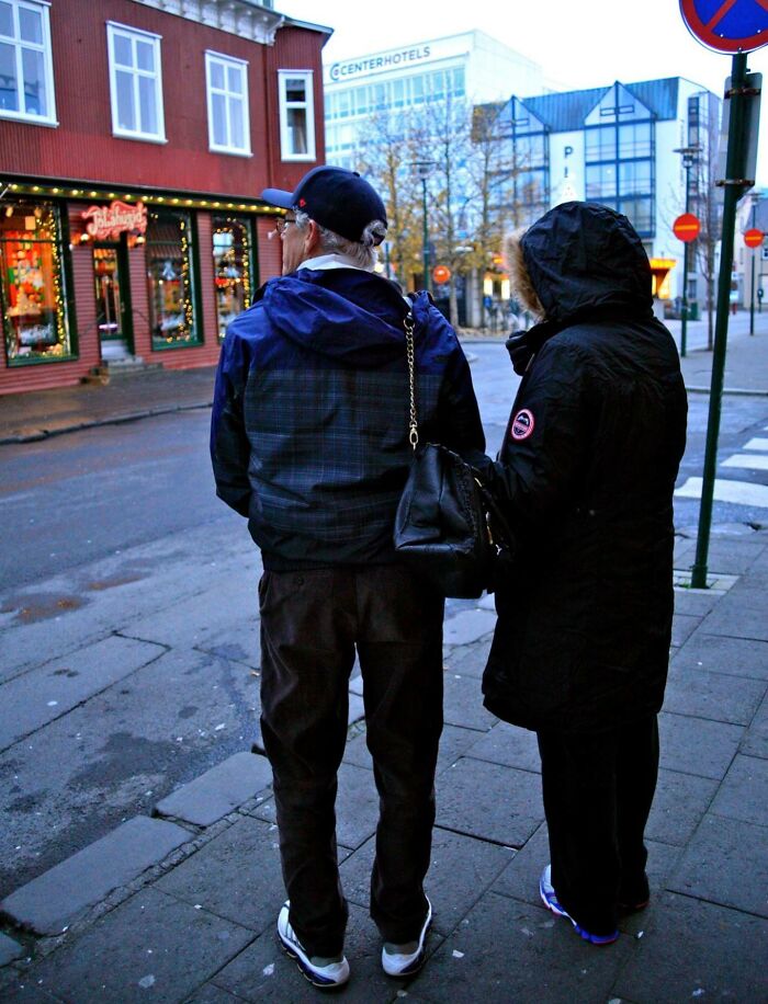 Two parents dressed for cold weather standing on a city sidewalk, capturing a funny and wholesome moment outdoors.