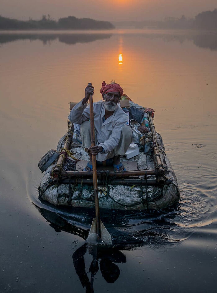 Elderly man rowing a rustic raft at sunrise, capturing everyday life in India on a calm river.