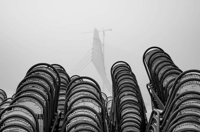 Stacked chairs in foggy outdoor scene with a modern bridge under construction, capturing everyday life in India.