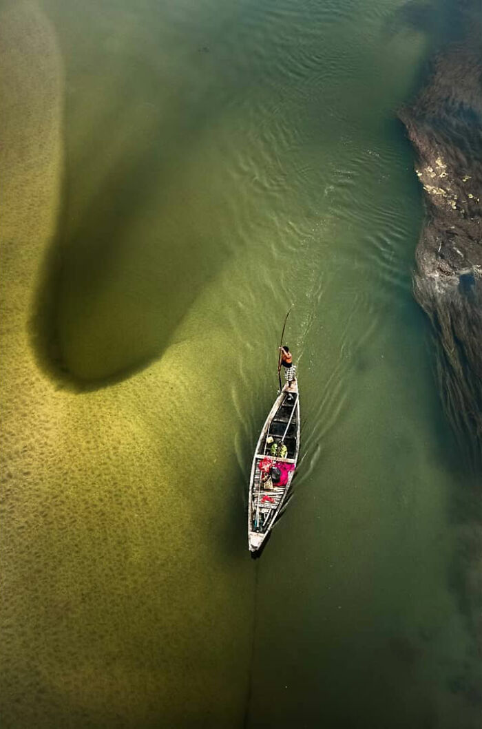 Aerial view of a boat with people navigating green and yellow waters showcasing everyday life in India.