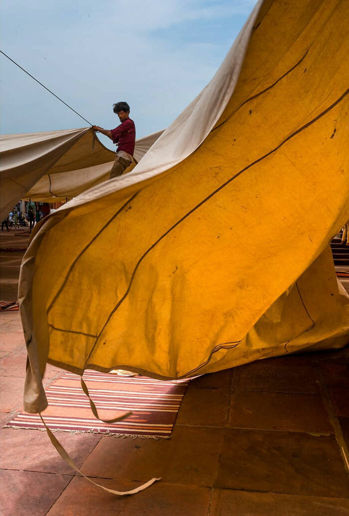 Man adjusting large yellow fabric outdoors, capturing everyday life in India with vibrant colors and dynamic movement.