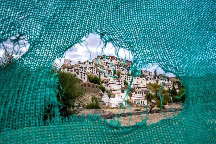 View of traditional Indian village architecture captured through a torn blue fabric, showcasing everyday life in India.