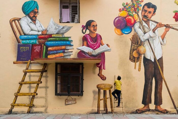 Colorful street art depicting everyday life in India with a man reading, a girl with a book, and a balloon seller on a wall.