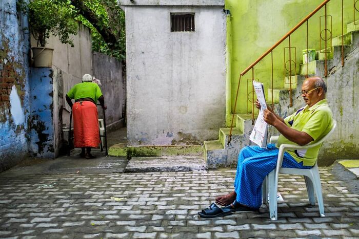 Elderly man reading newspaper and woman walking with walker in a colorful courtyard capturing everyday life in India.