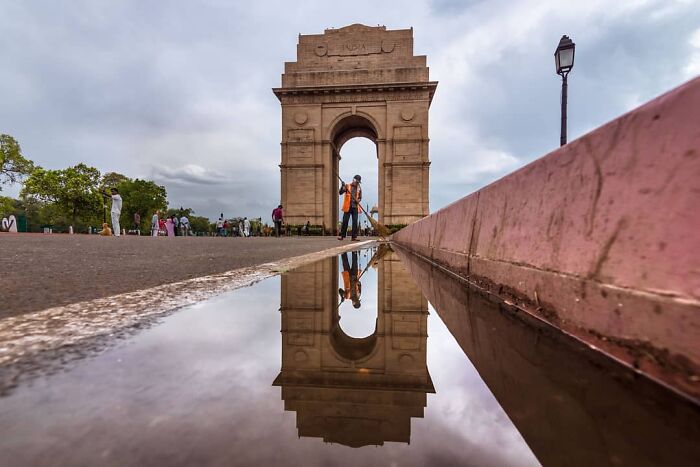 India Gate reflected in water with a street cleaner sweeping, capturing everyday life in India.