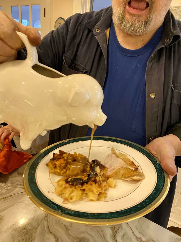 Man pouring gravy from a pig-shaped pitcher onto a Thanksgiving plate, showcasing funny and wholesome parents moments.