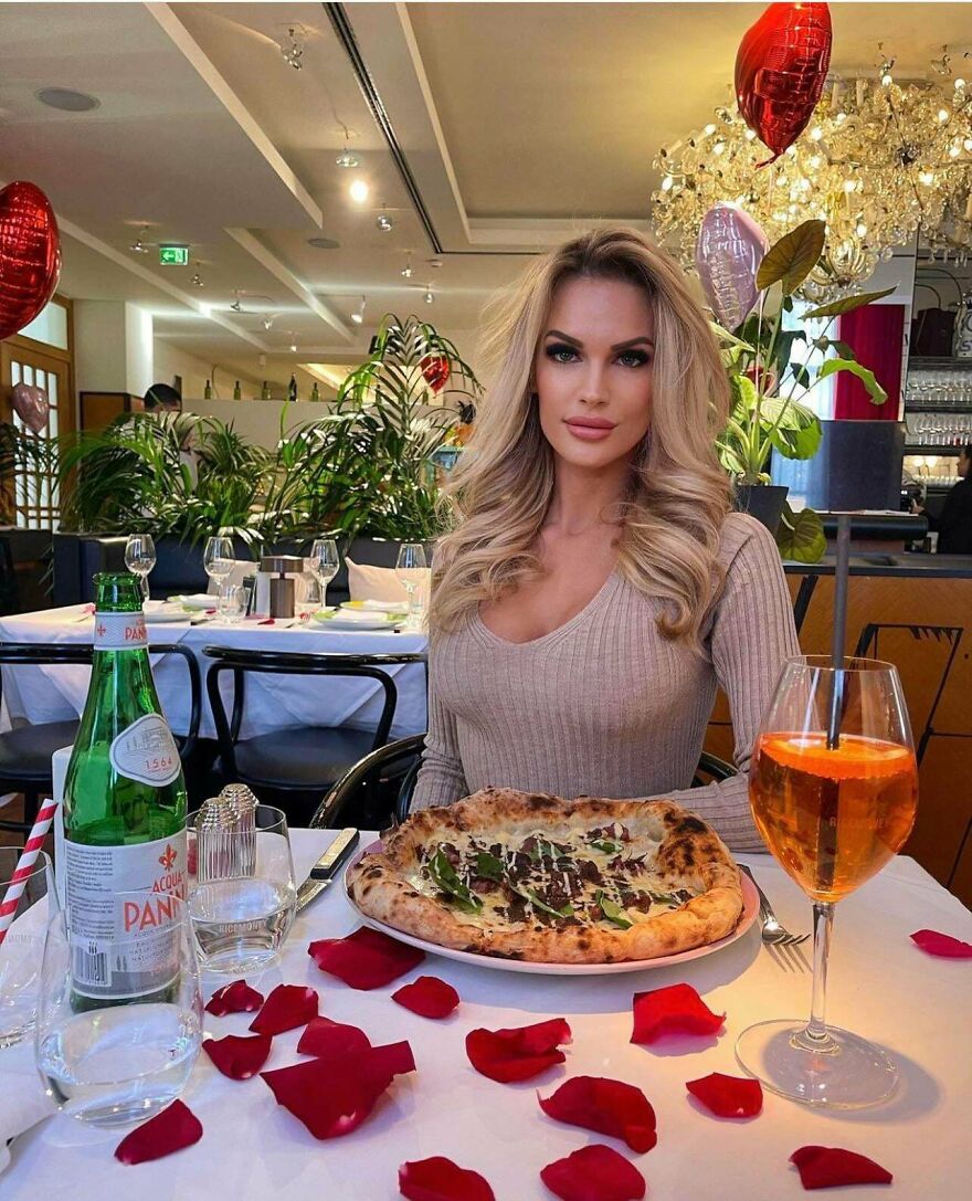 Mujer en restaurante con pizza y bebida, mostrando belleza real y natural m&aacute;s all&aacute; de Instagram.
