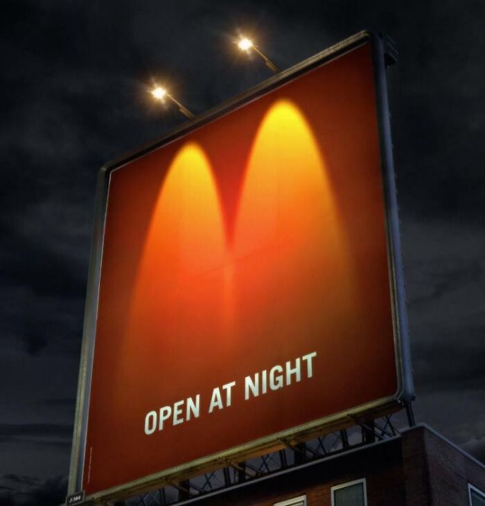 Billboard at night with "Open at night" text illuminated by two yellow lights, showcasing funny and weird billboards.