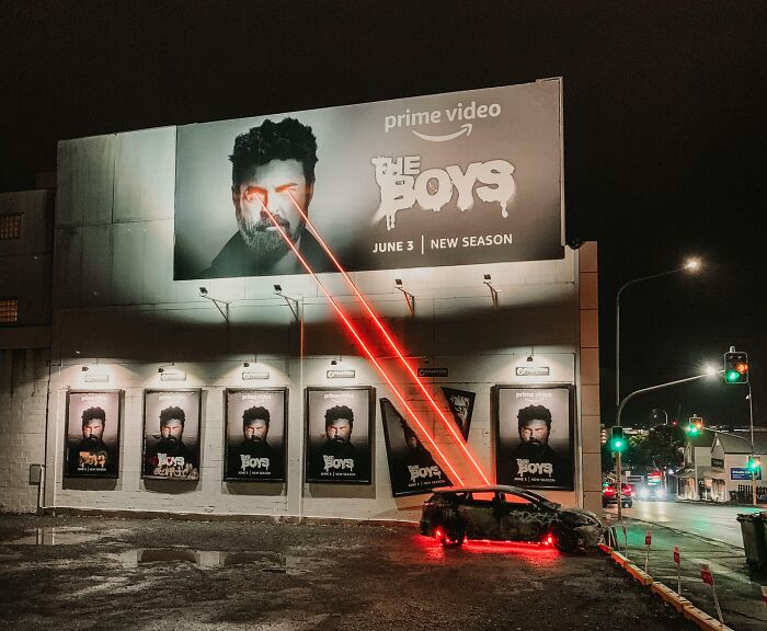 Billboard with a face shooting red laser beams from eyes at a car, showcasing funny and weird billboards at night.