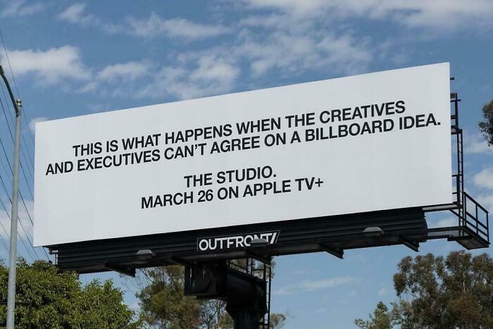 Billboard with a humorous message about creatives and executives disagreeing on a billboard idea under a blue sky.
